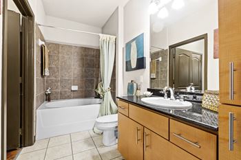 bathroom with warm wood cabinets, toilet and bathtub with brown tiles